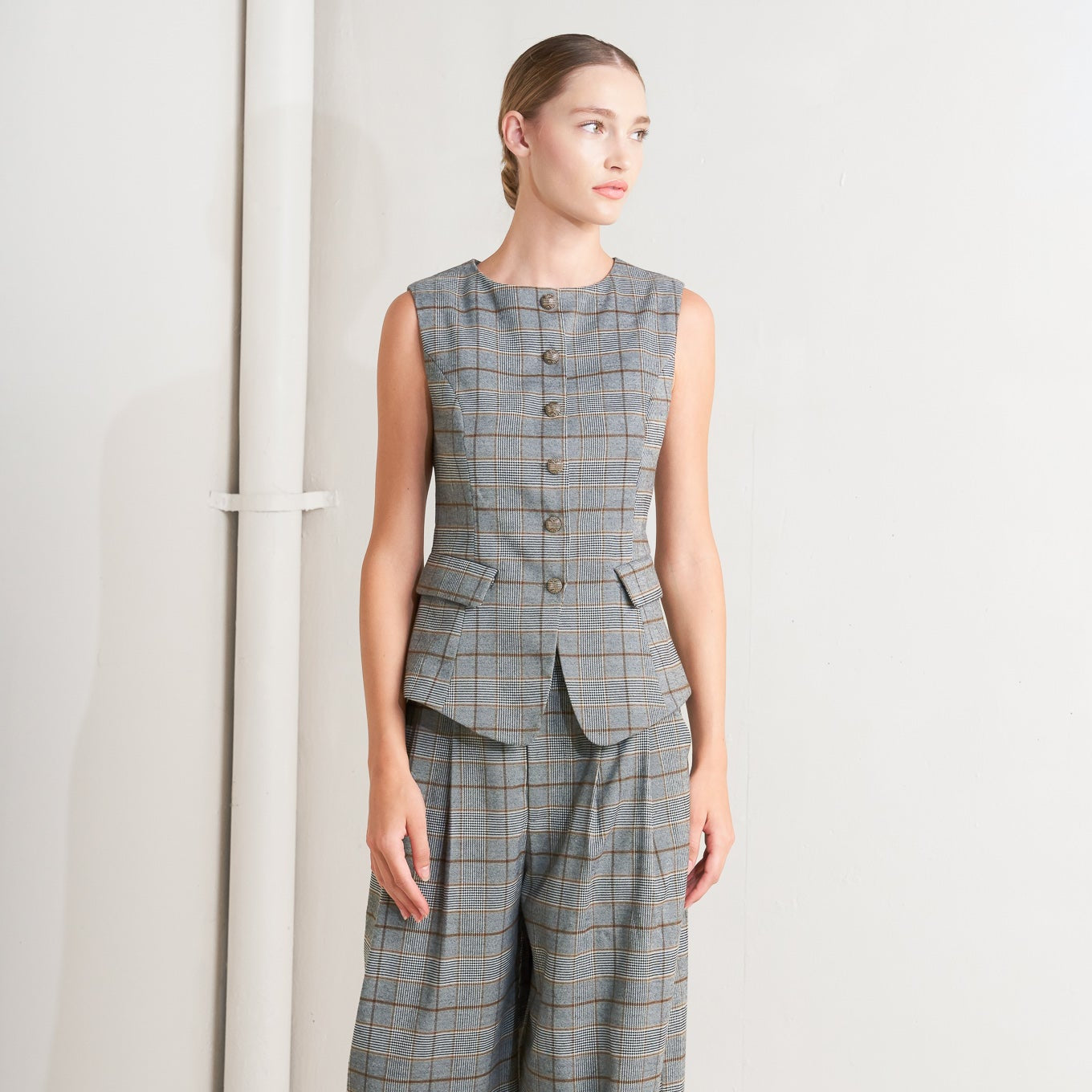 Woman wearing a gray plaid sleeveless top and wide-leg pants against a white background