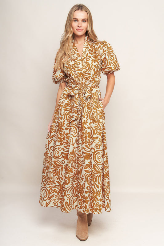 Woman wearing a camel color floral patterned maxi dress against a plain background