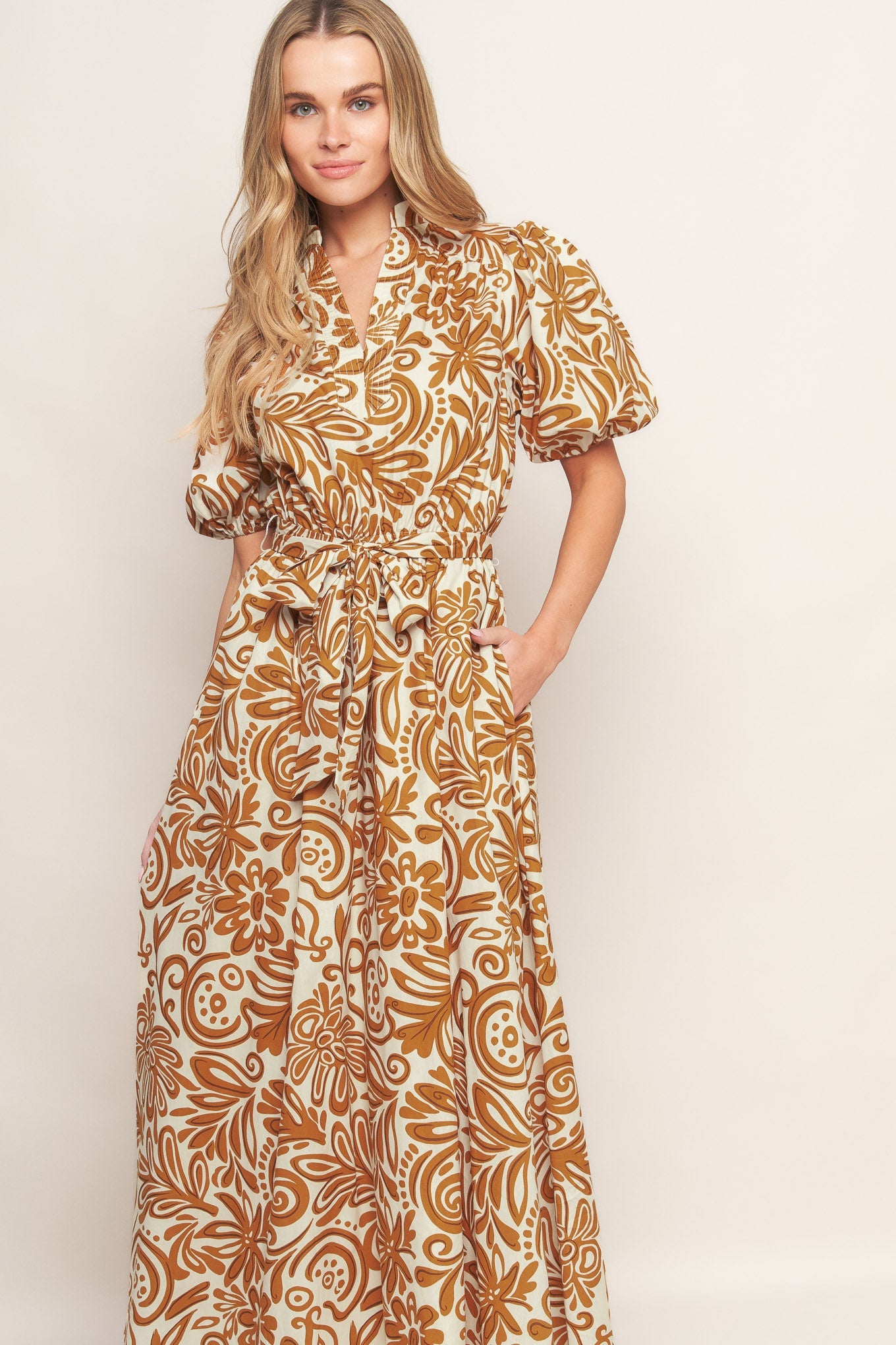 Woman wearing a camel color floral patterned maxi dress with puffed sleeves against a plain background