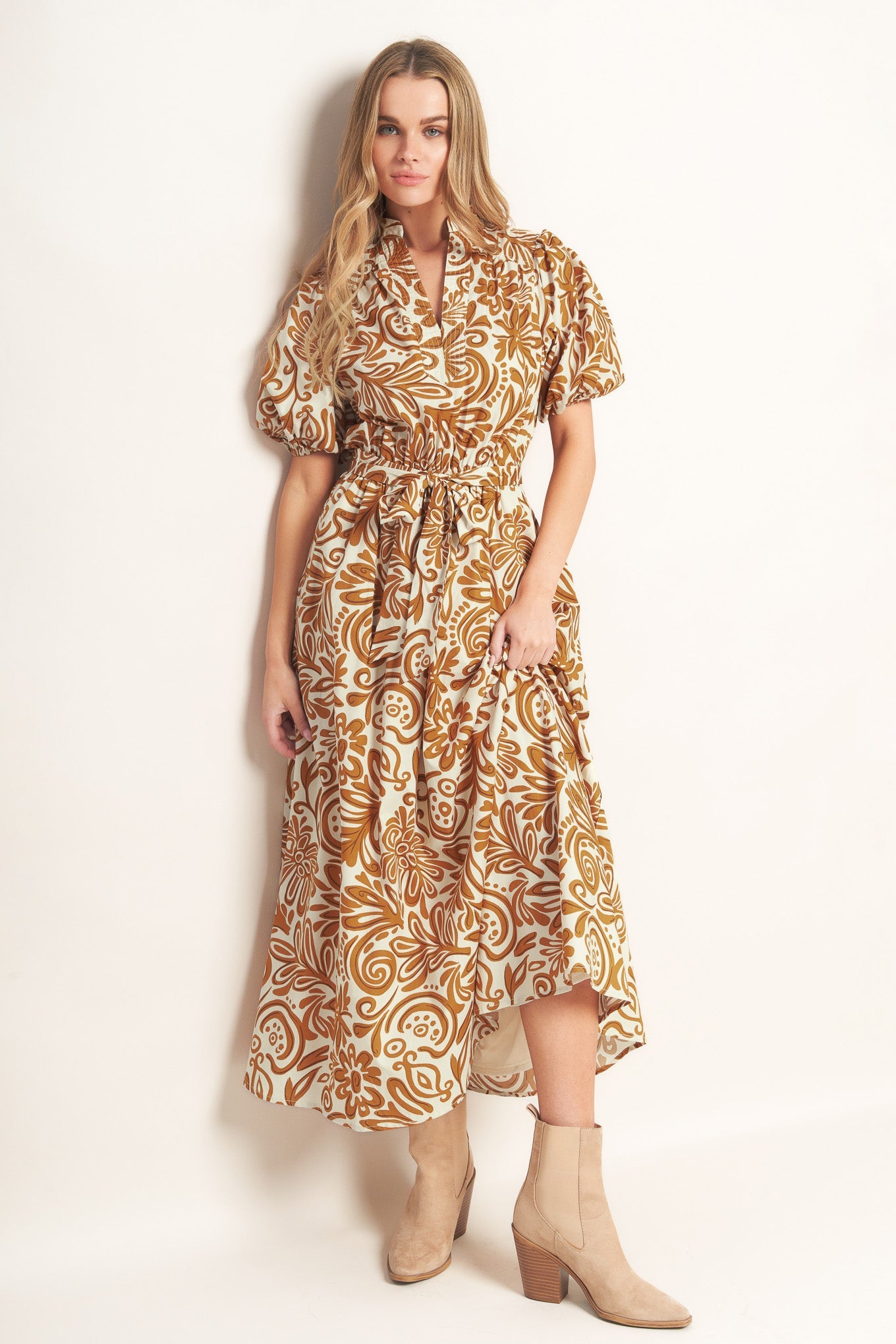 Woman wearing a camel color floral patterned maxi dress against a plain background