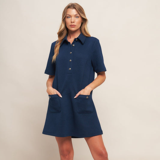 Woman wearing a navy blue dress with short sleeves and pockets on a beige background