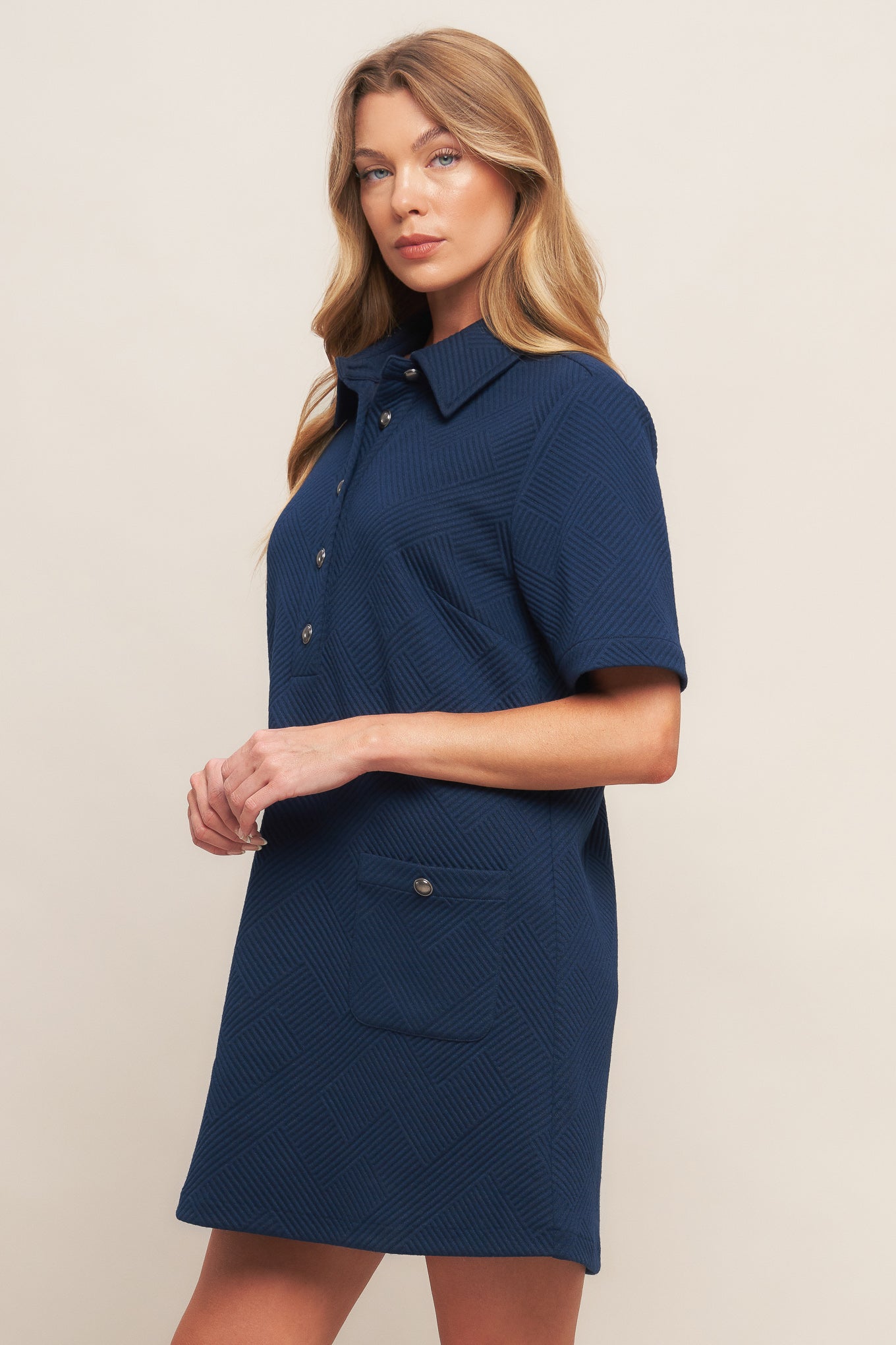 Woman wearing a navy blue dress with short sleeves and a collar on a beige background