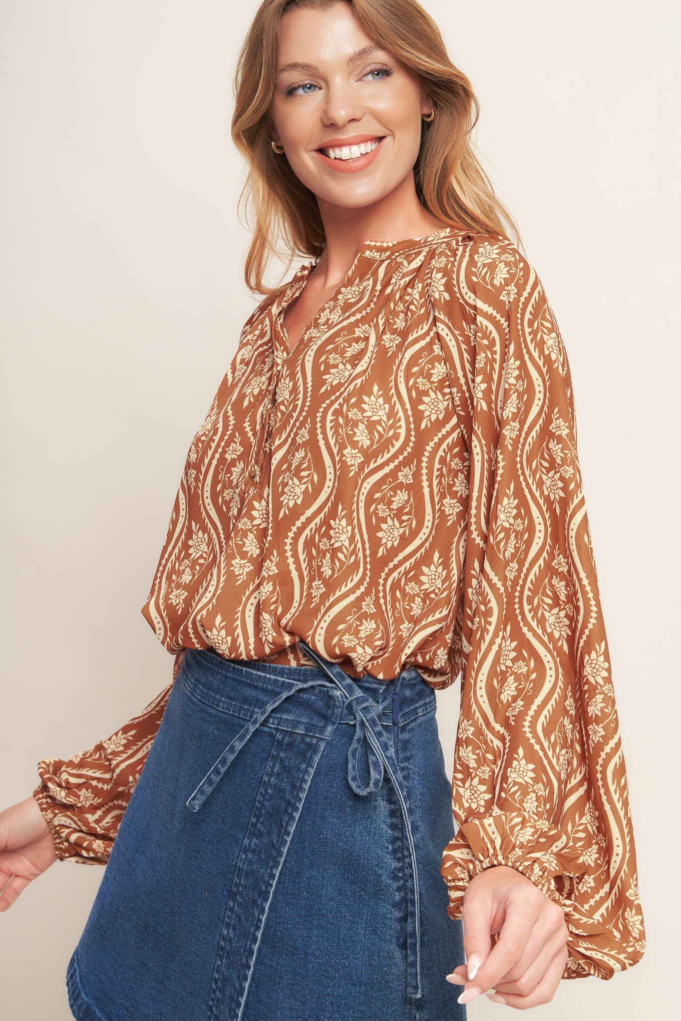 Woman wearing a patterned blouse and denim skirt against a plain background