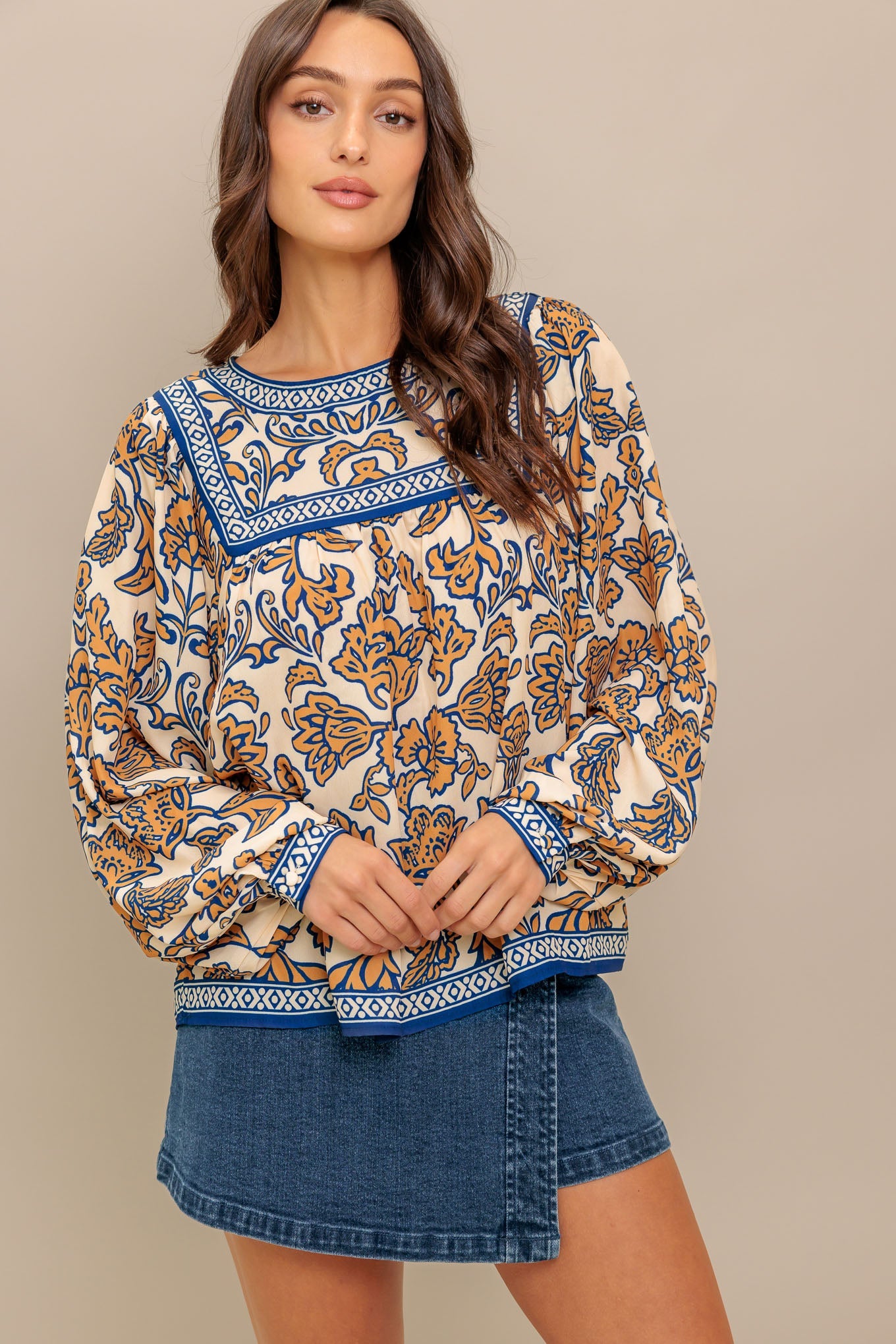 Woman wearing a patterned top and denim shorts on a beige background