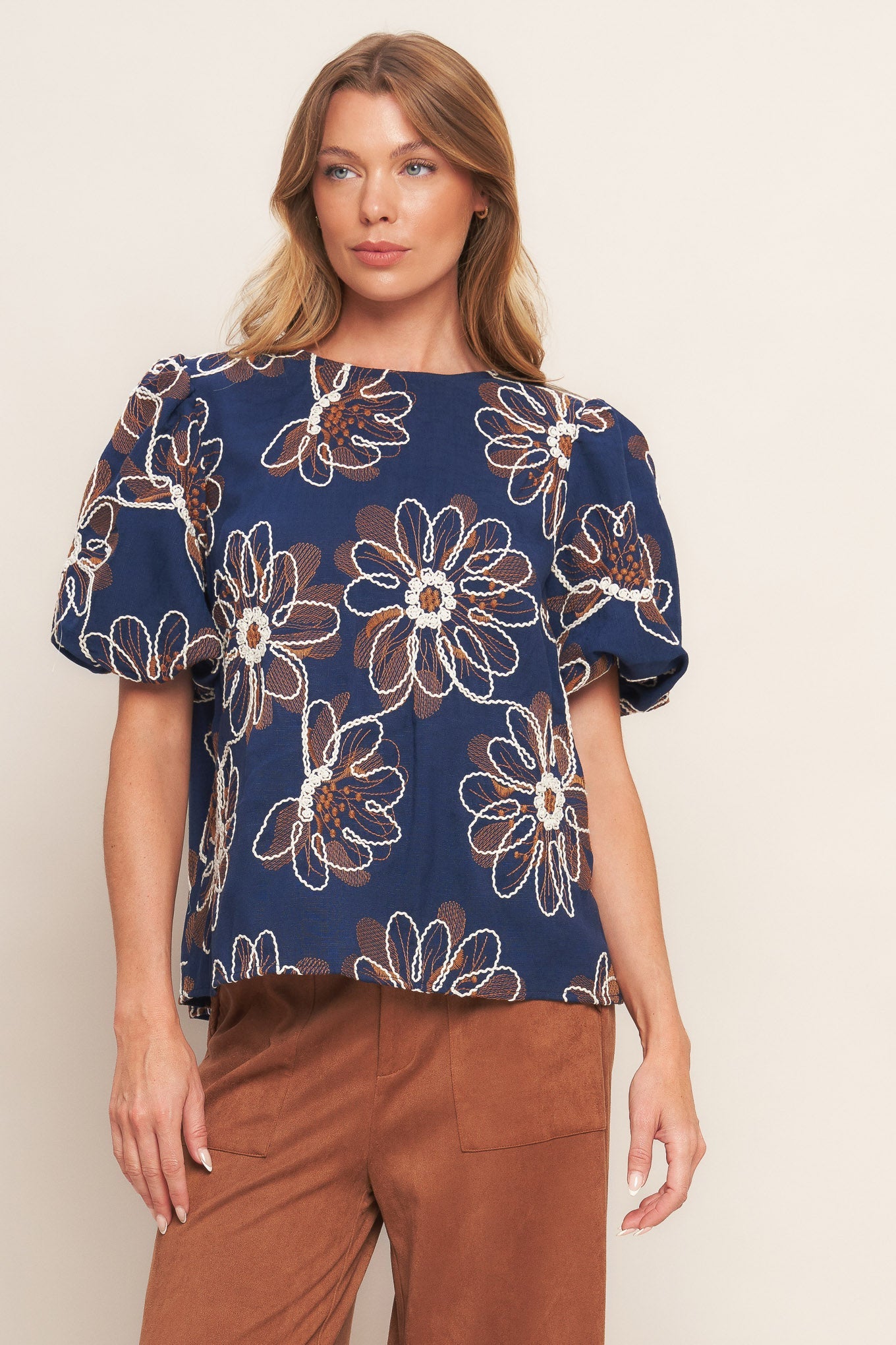 Woman wearing a navy blue floral blouse with brown pants on a beige background
