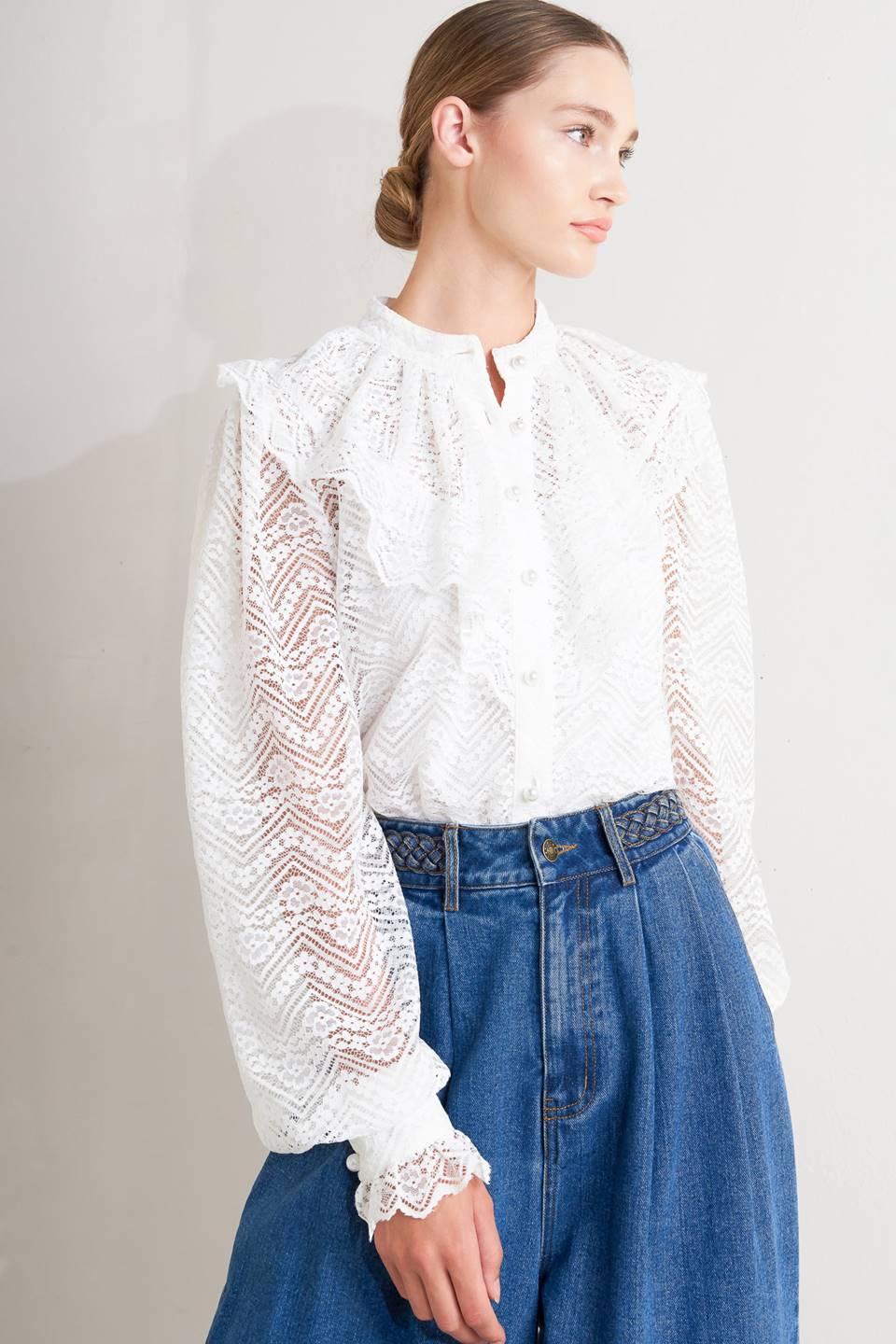 Woman wearing a white lace blouse and blue jeans against a plain background
