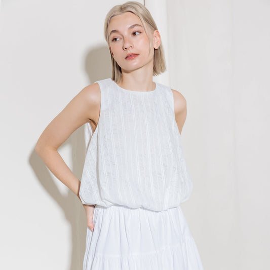 A women wearing a white eyelet lace sleeveless top with bubble hem and round neckline for beach and summer casual wear