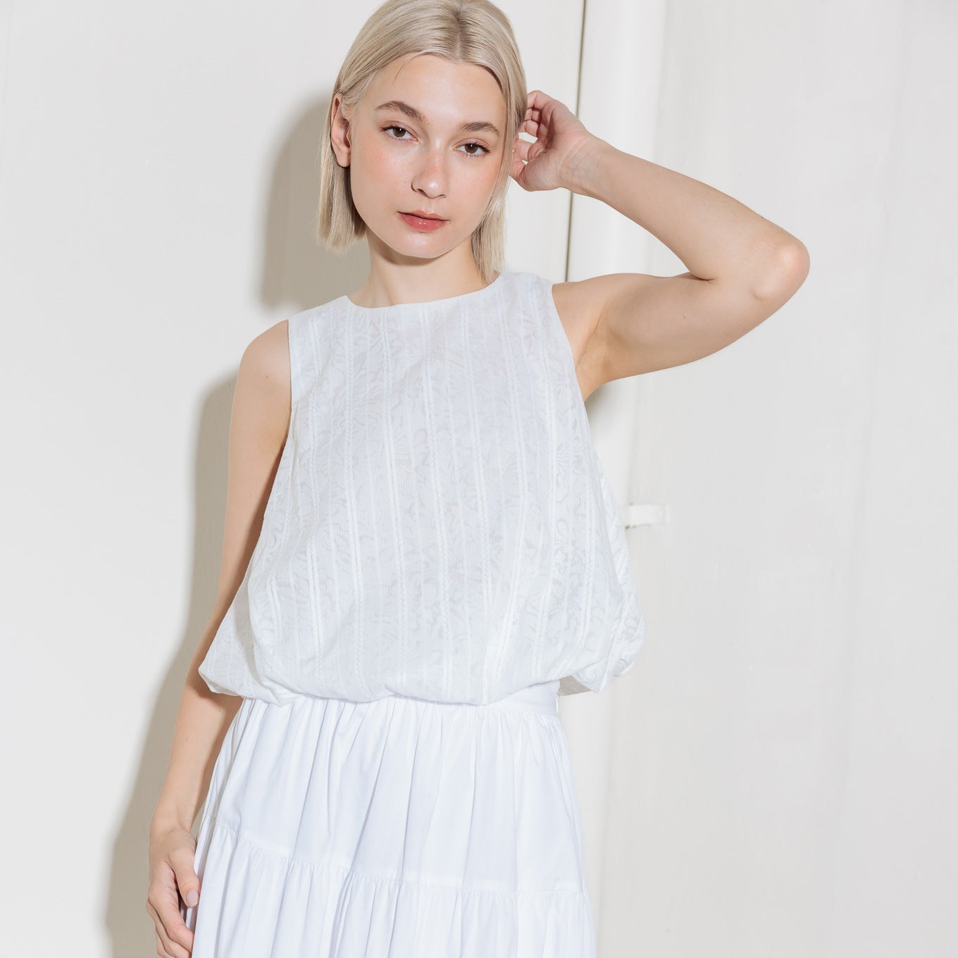 Woman wearing a white sleeveless top and pleated skirt against a plain background