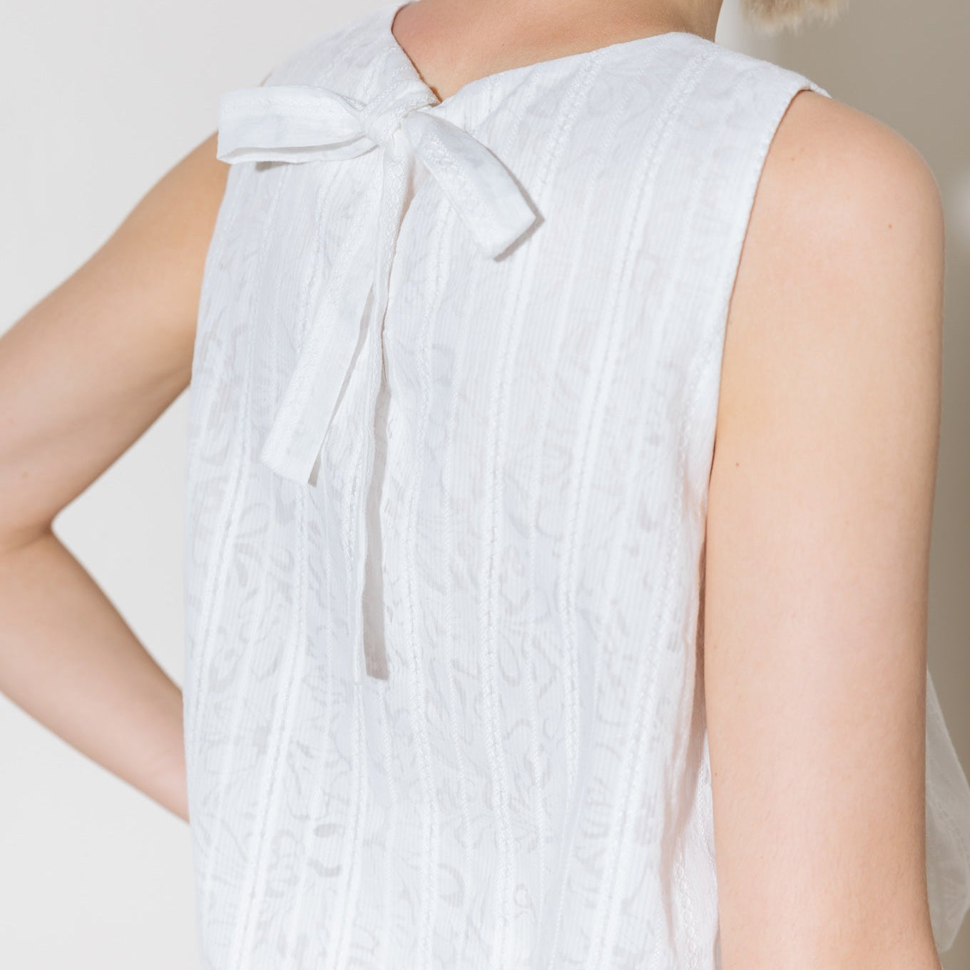 A women wearing a white eyelet lace sleeveless top with bubble hem and round neckline for beach and summer casual wear With a bow detail in the back