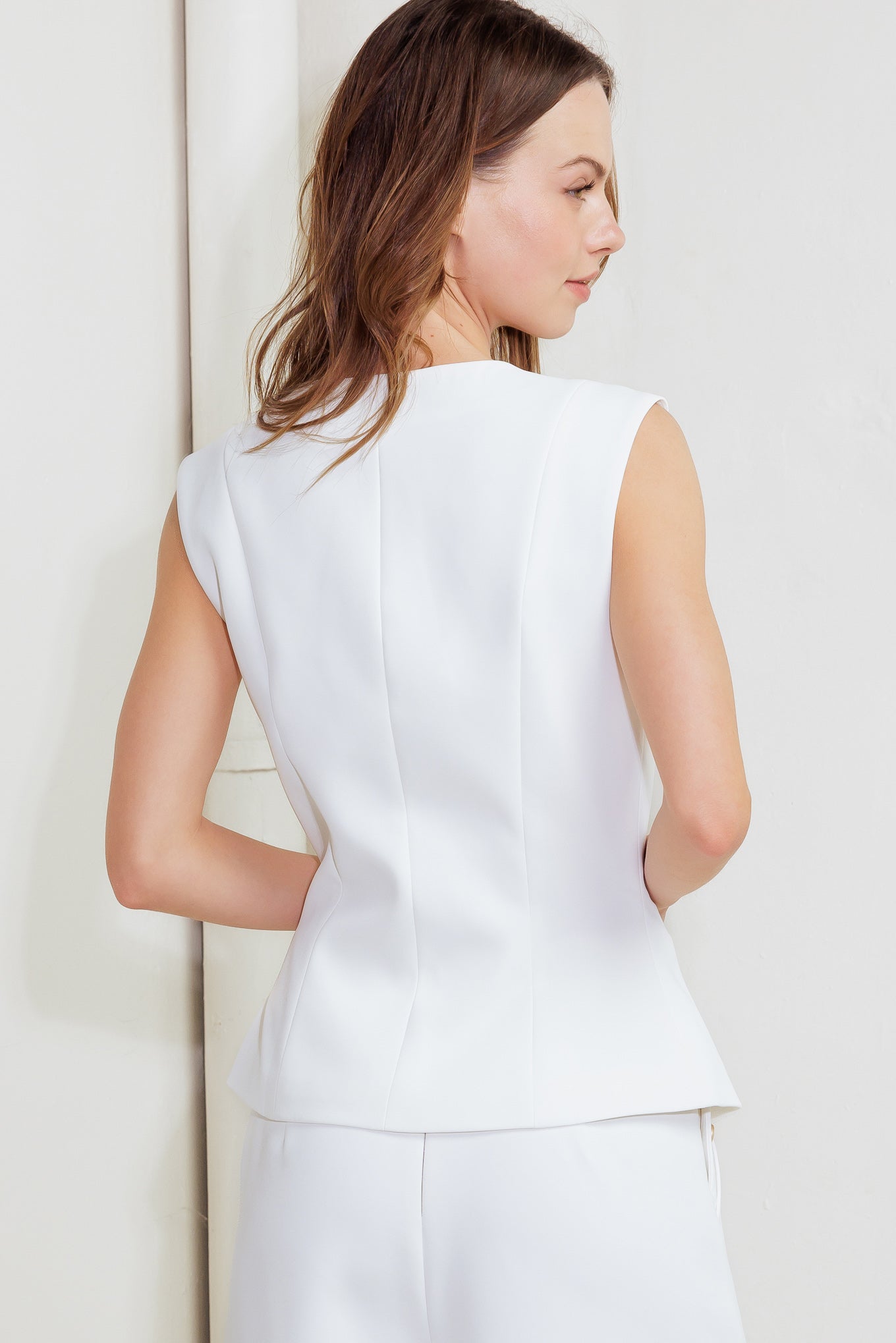 Woman wearing a white sleeveless vest and pants against a light background
