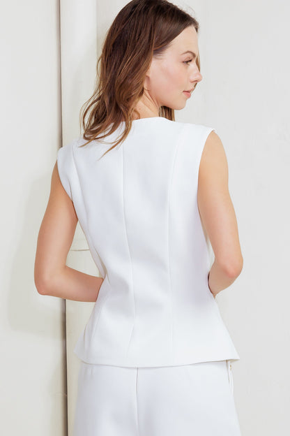 Woman wearing a white sleeveless vest and pants against a light background