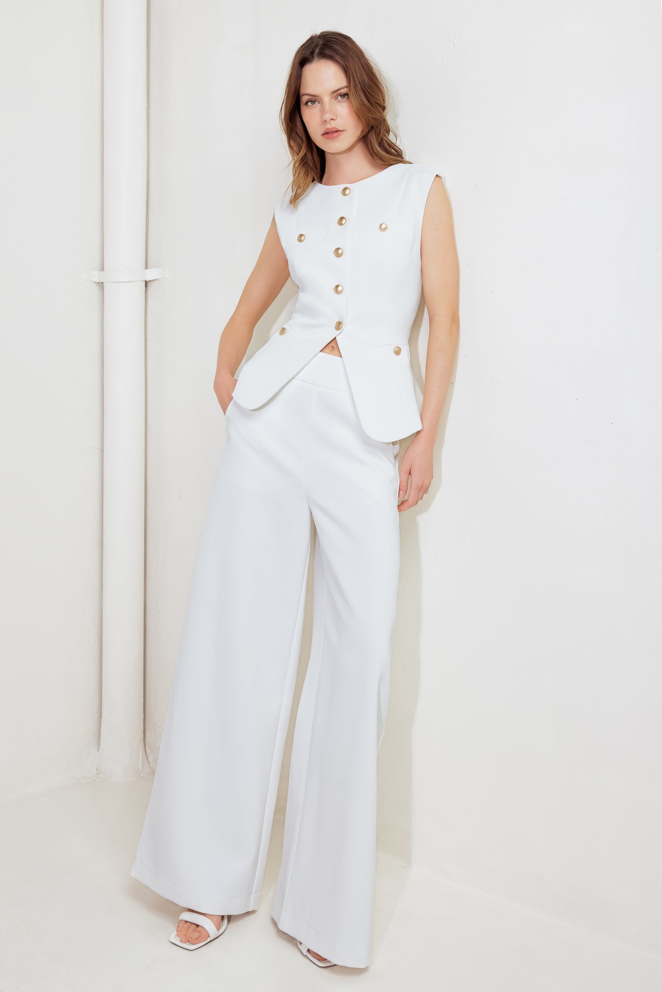 Woman wearing a white outfit with gold buttons against a plain background