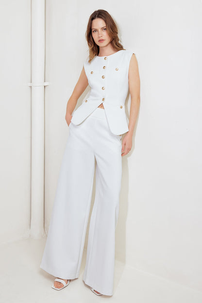 Woman wearing a white outfit with gold buttons against a plain background