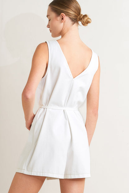 Woman wearing a white sleeveless romper with a V-neckline back on a plain background