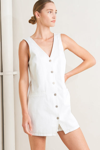 Woman wearing a white sleeveless romper with buttons on a plain background