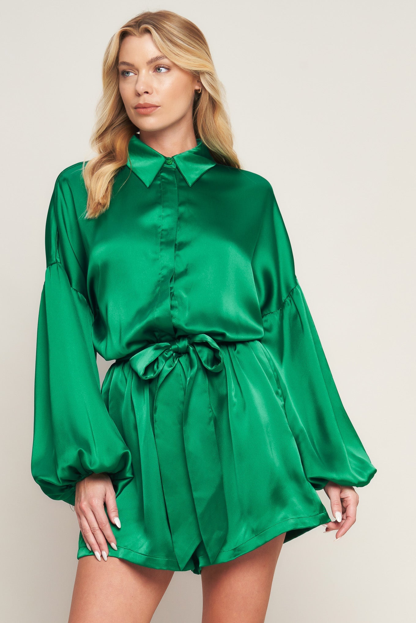 Emerald green satin romper with bishop sleeves, shirt collar, and tie waist for holiday celebrations and special events