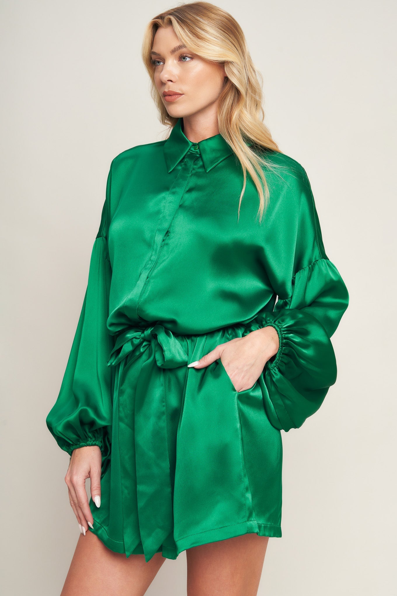 Emerald green satin romper with bishop sleeves, shirt collar, and tie waist for holiday celebrations and special events
