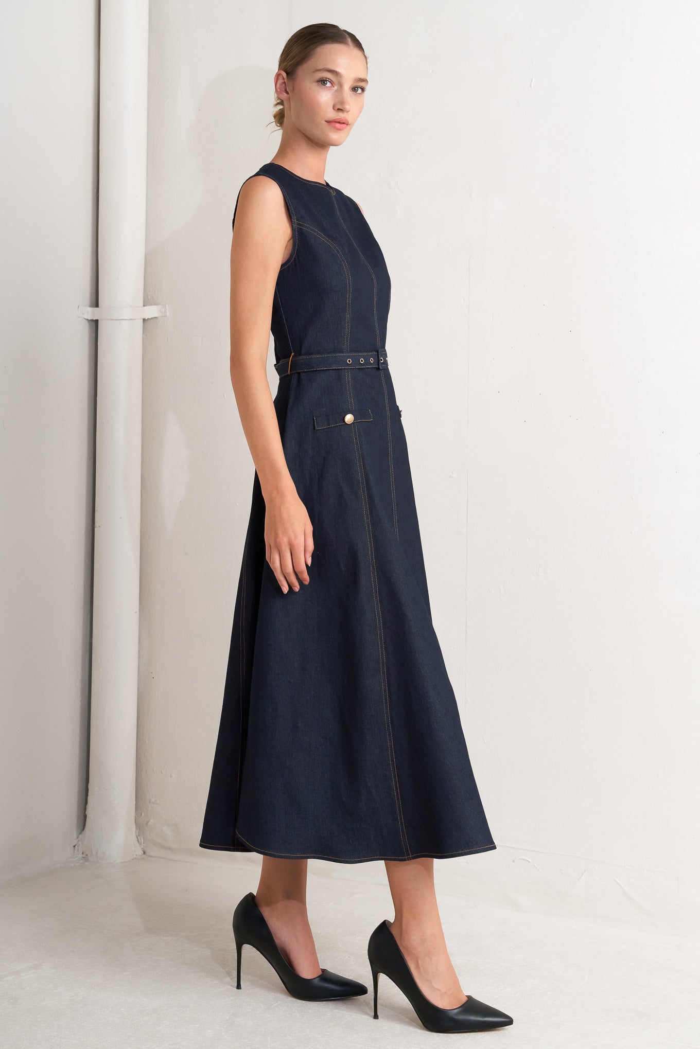 Woman wearing a navy blue sleeveless dress with a belt against a white background