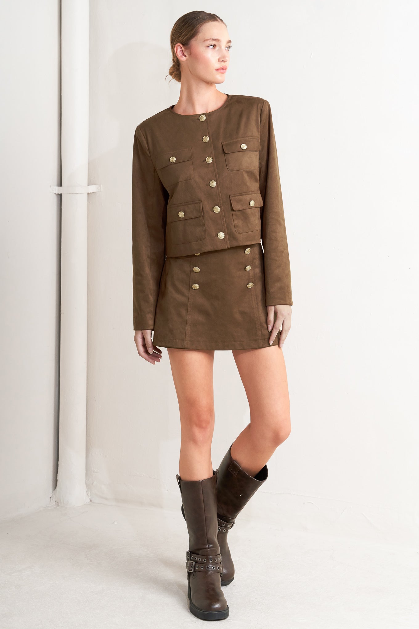 Woman wearing a brown military-style jacket and skirt with boots on a white background