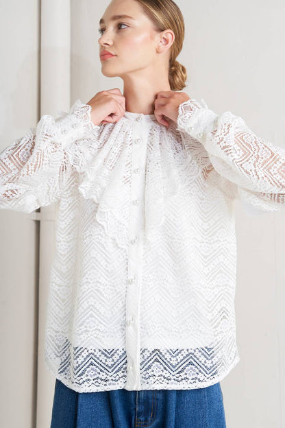 Woman wearing a white lace blouse with long sleeves against a plain background