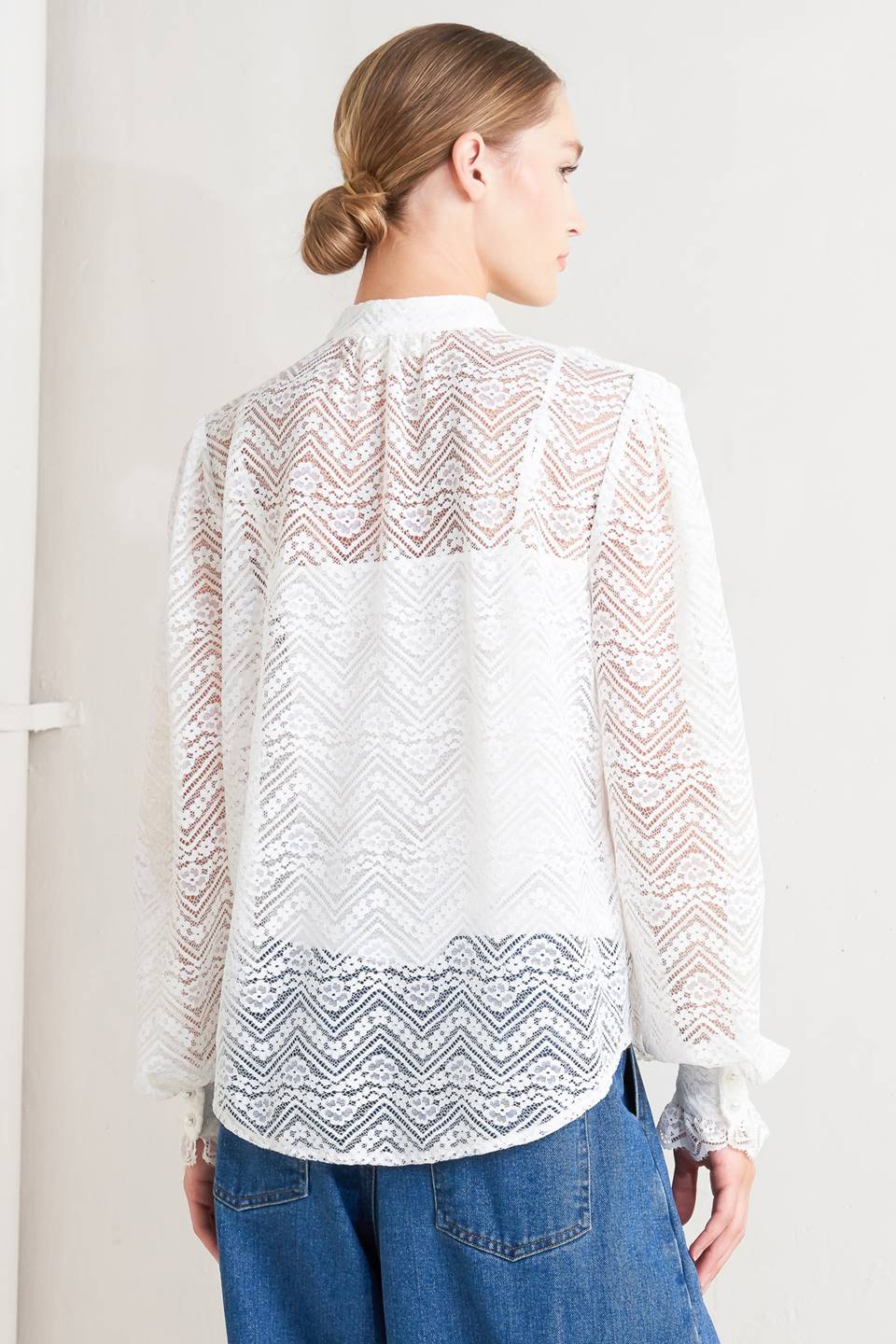 Woman wearing a white lace blouse with a plain background