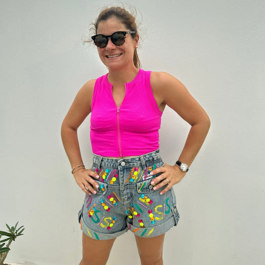 A person wearing hand painted denim shorts with a high-rise waist and colorful bead details, paired with a pink sleeveless top.