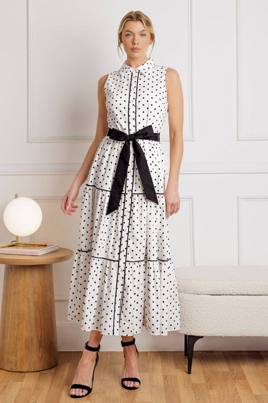Woman wearing a polka dot dress with a black belt in a room setting.