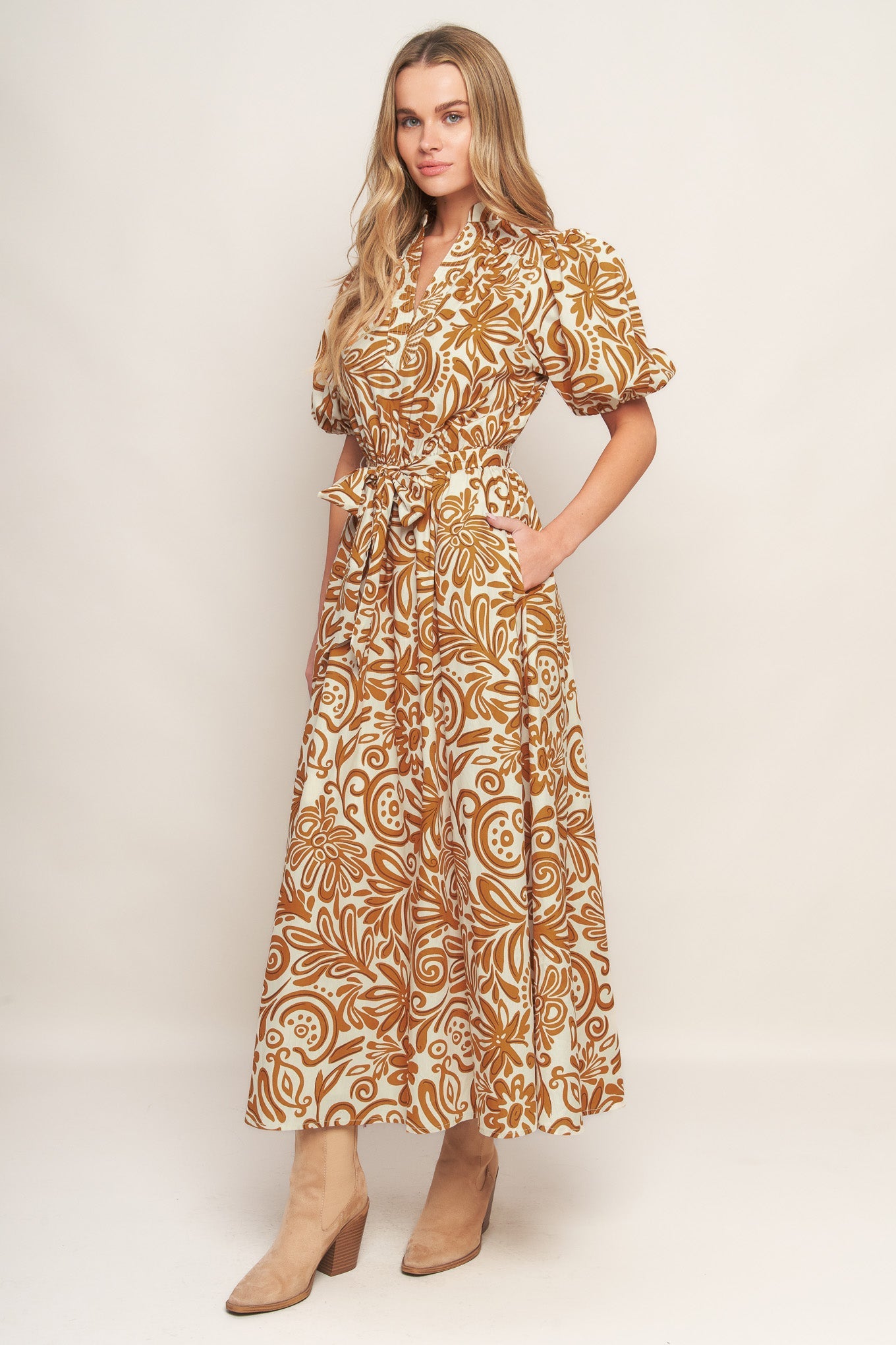 Woman wearing a camel color floral patterned maxi dress with puffed sleeves against a plain background