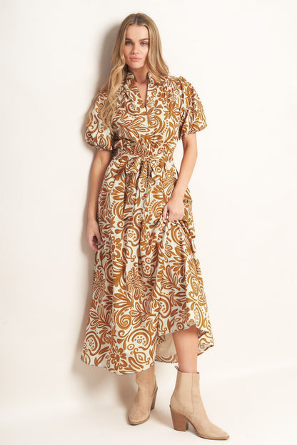 Woman wearing a camel color floral patterned maxi dress against a plain background