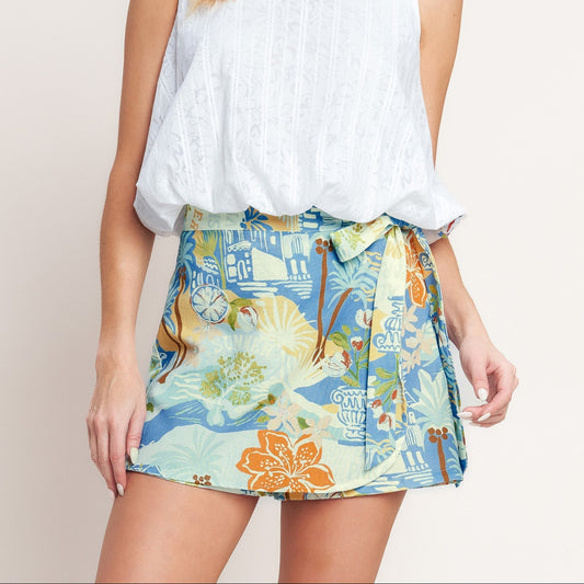 Woman wearing a white top and colorful floral skirt against a plain background