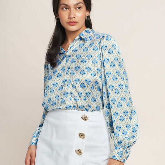Woman wearing a blue floral blouse and white shorts with gold buttons on a beige background