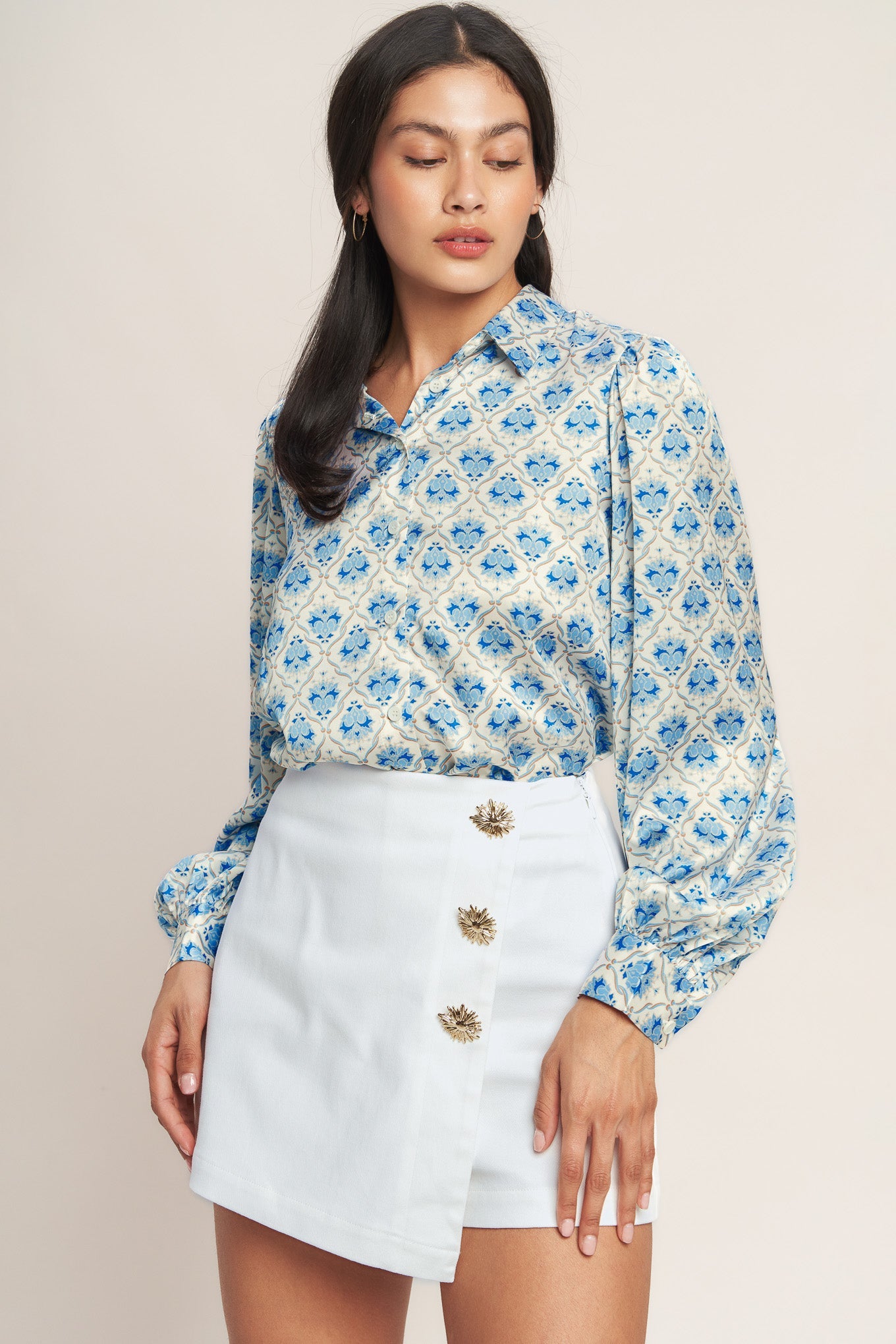 Woman wearing a blue patterned blouse and white skirt against a beige background