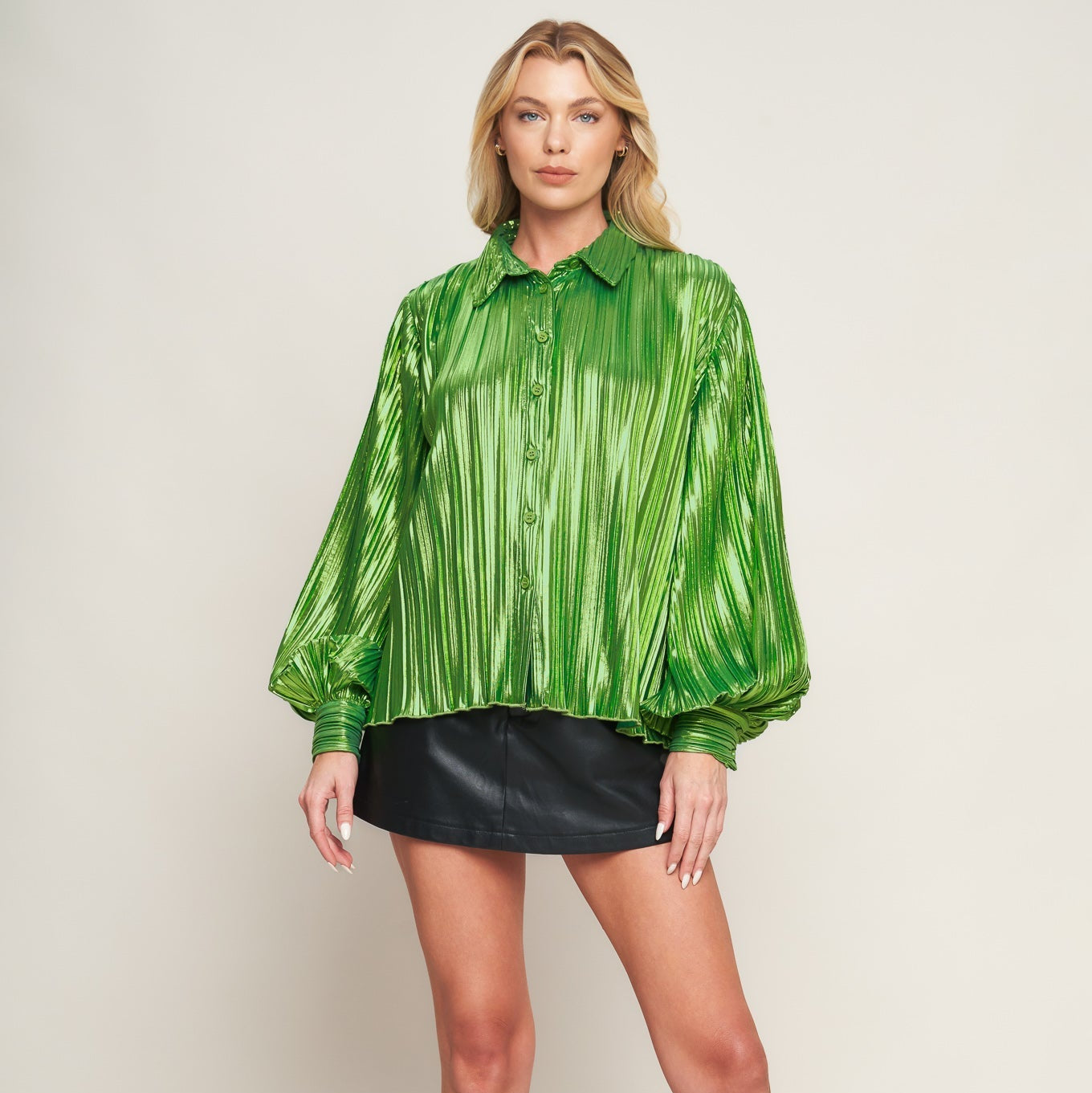 Person wearing a green metallic blouse, black leather skirt, and black boots on a white background