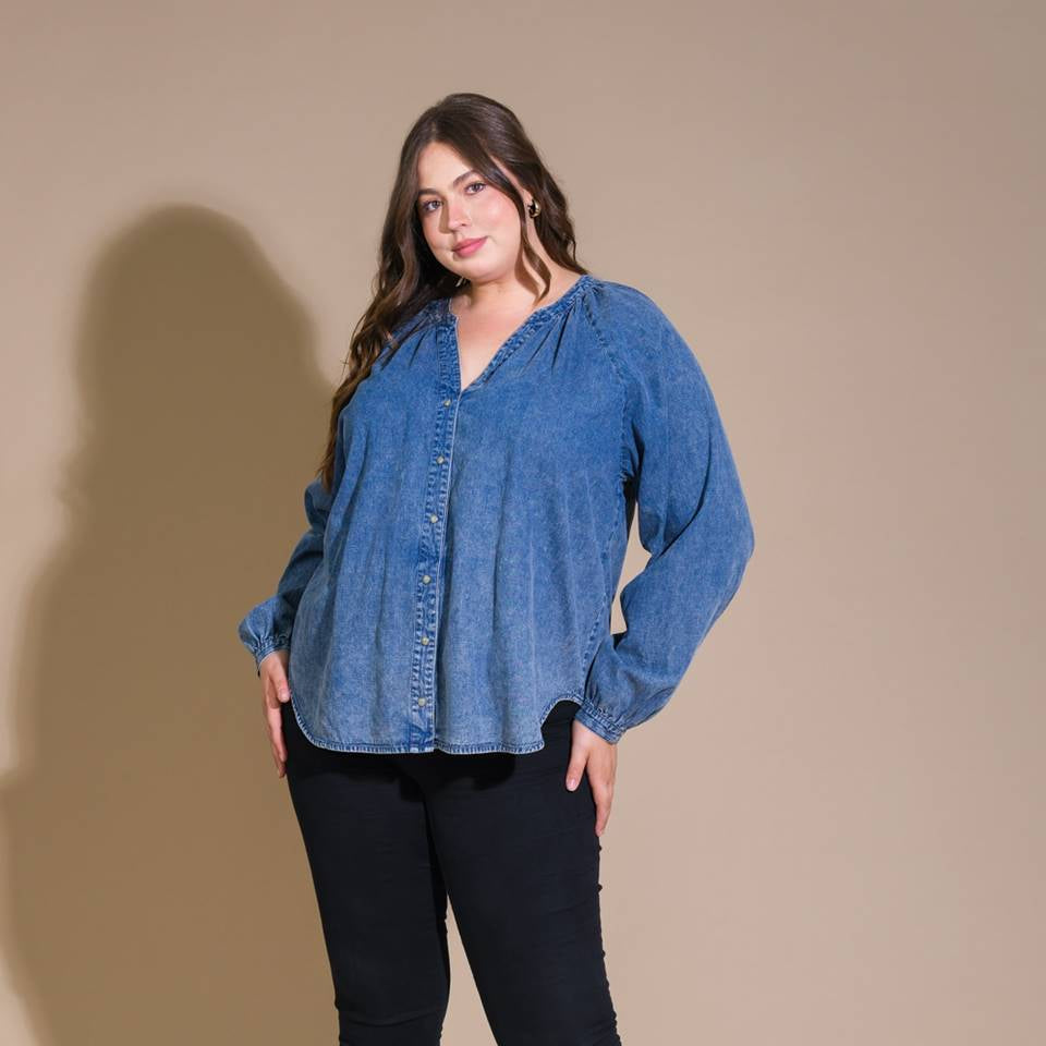Woman wearing a blue denim shirt and black pants against a beige background