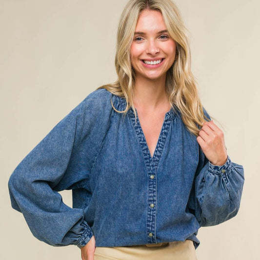 Woman wearing a blue denim blouse and beige skirt against a plain background