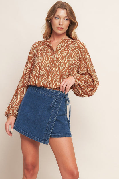 Woman wearing a patterned blouse and denim skirt against a beige background