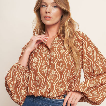 Woman wearing a patterned blouse and blue jeans against a beige background