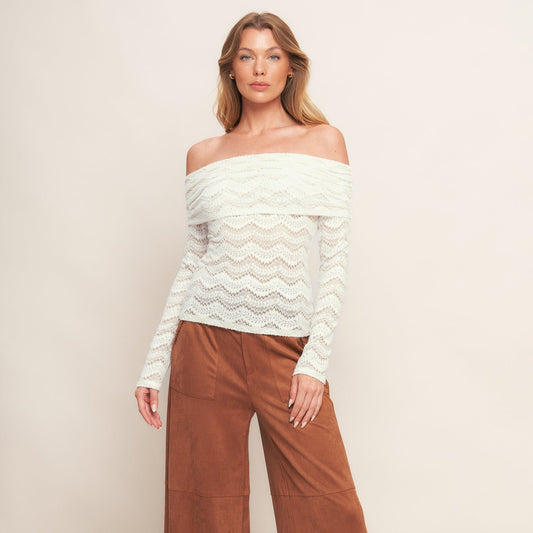 Woman wearing a white off-shoulder top and brown wide-leg pants on a plain background