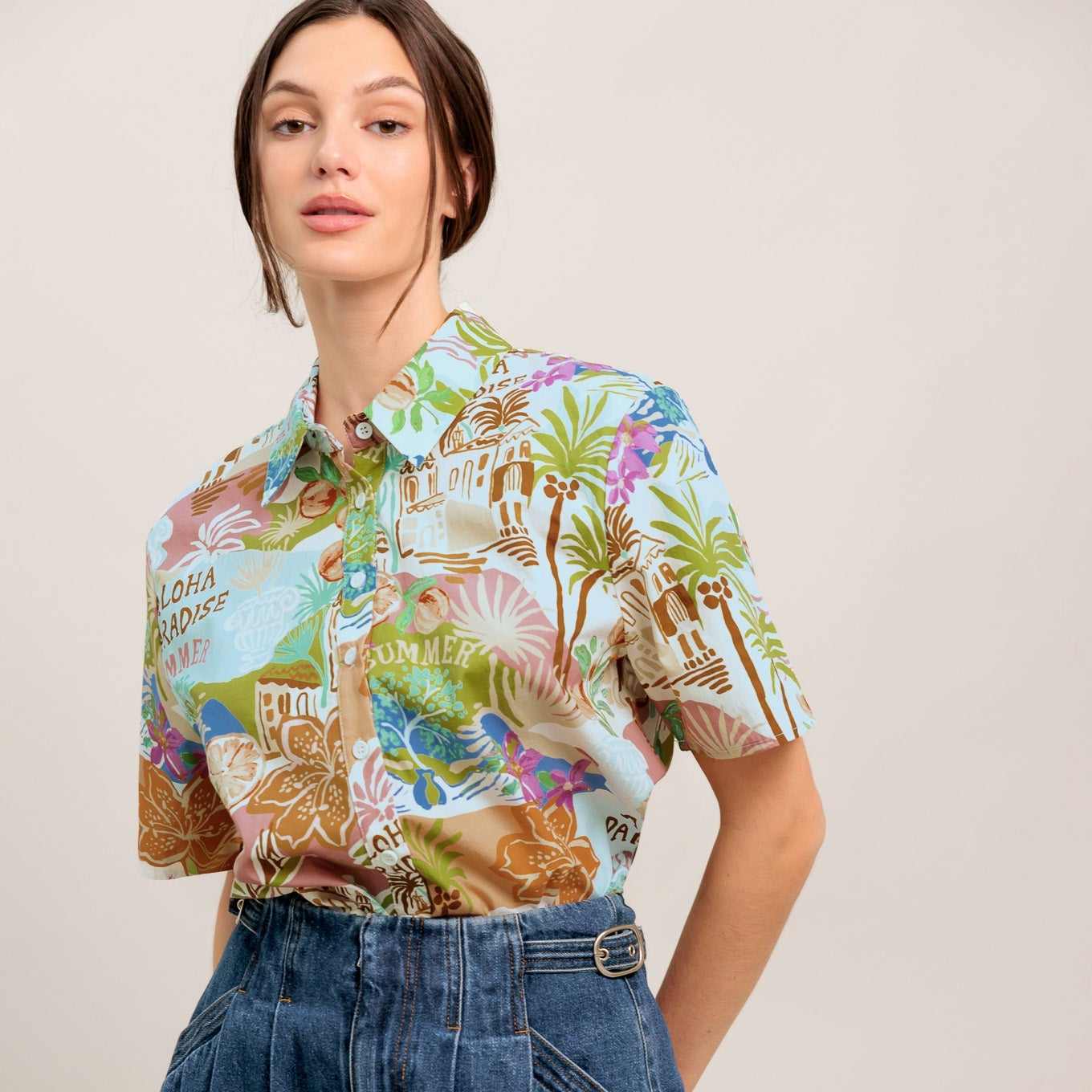 Woman wearing a colorful patterned shirt and denim shorts on a plain background