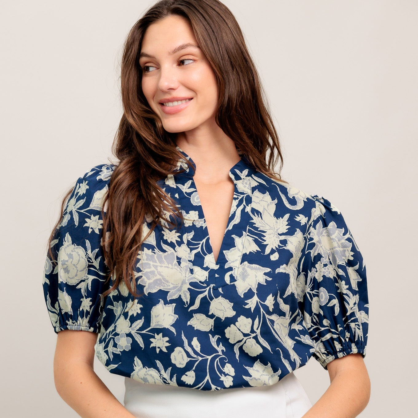 Woman wearing a blue floral blouse and white skirt on a plain background