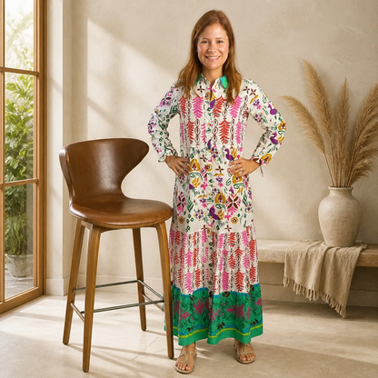Woman wearing ivory full-length cotton maxi dress with multicolor folk print in pink, purple, orange and green with teal border hem, Chinese collar and long sleeves, styled with nude sandals