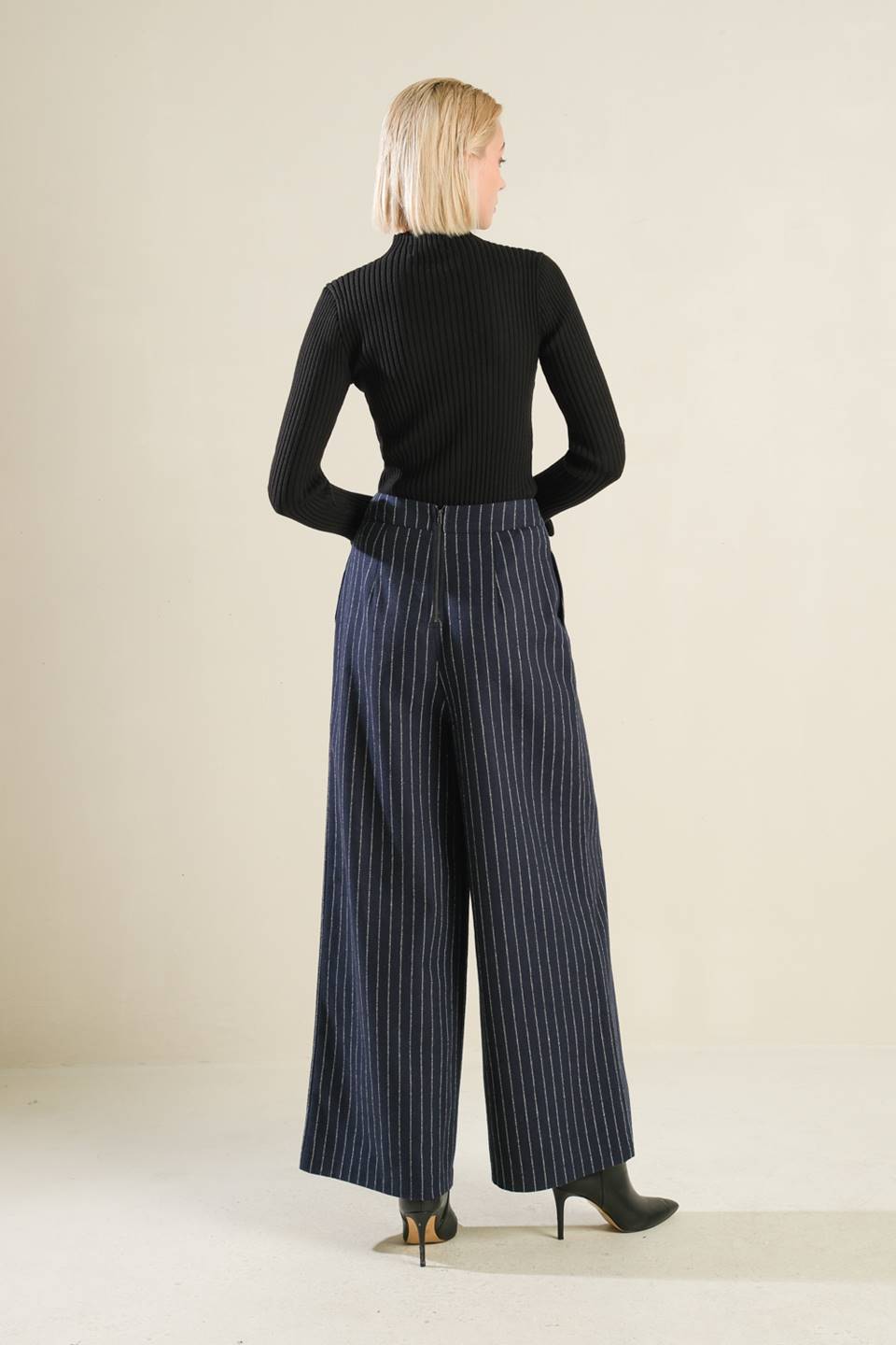 Woman wearing a black top and blue pinstripe pants on a beige background
