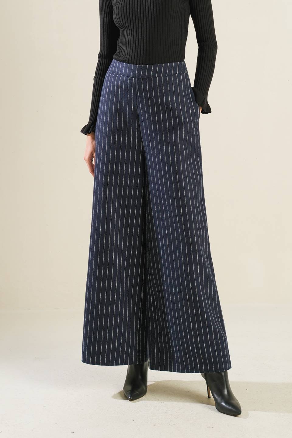 Person wearing black pinstripe pants and a black top on a beige background