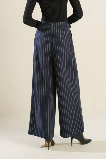 Person wearing black ribbed sweater and blue pinstripe pants on a plain background