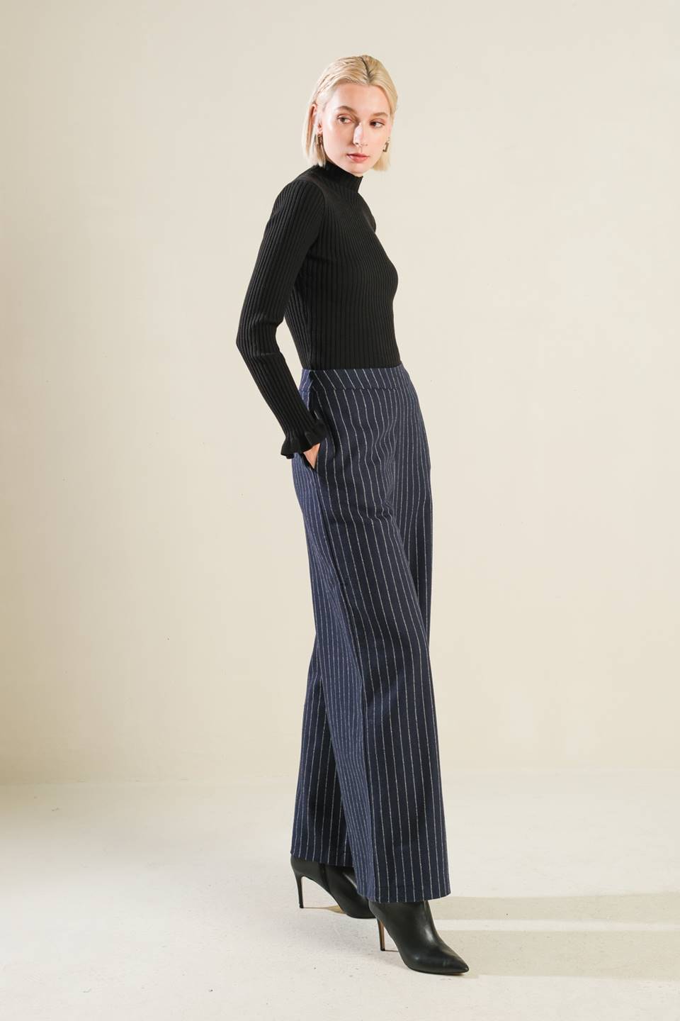 Woman wearing a black turtleneck and blue striped pants on a beige background