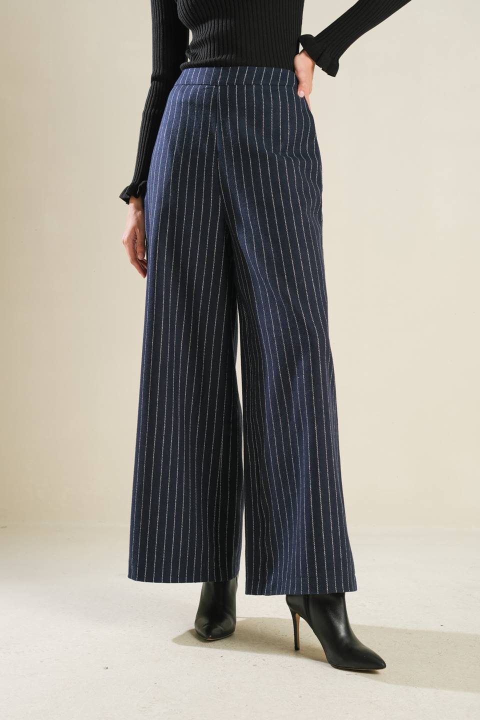 Person wearing blue pinstripe pants and black top on a plain background