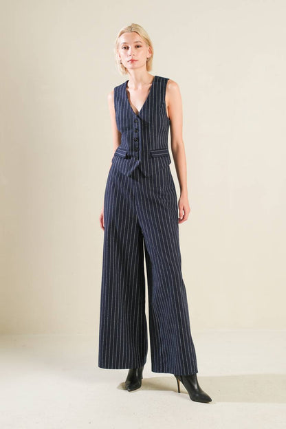 Woman wearing a navy pinstripe jumpsuit on a beige background