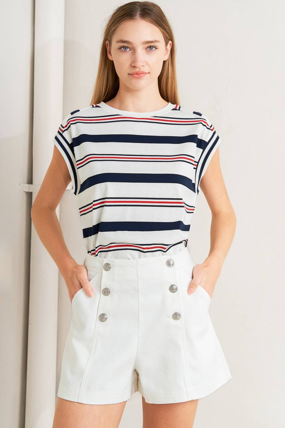 Woman wearing a striped shirt and white shorts with button details on a plain background