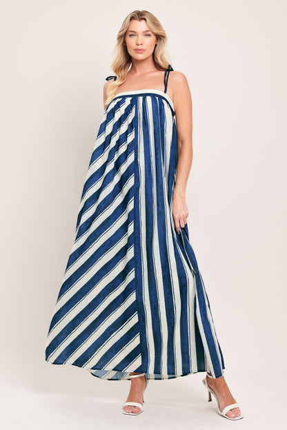Woman wearing navy and ivory striped maxi dress with shoulder ties and smocked back, styled with white heeled sandals