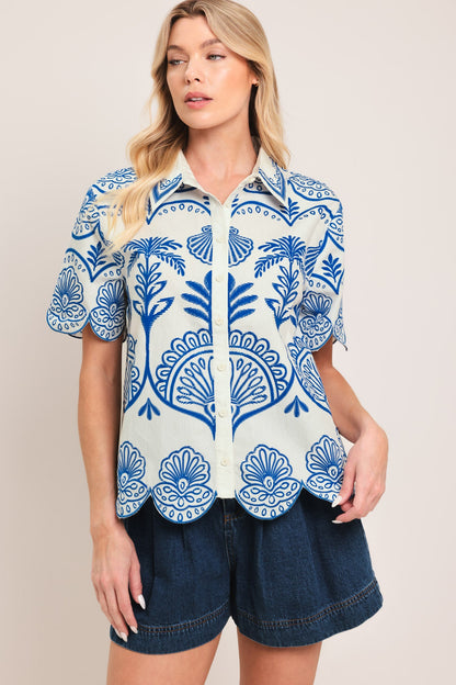 Woman wearing cobalt blue and ivory botanical print cotton button-down shirt with scalloped hem and sleeves, styled with dark denim shorts